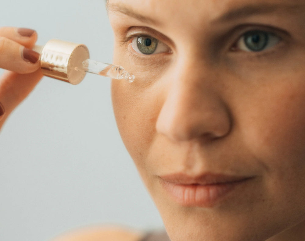 Frau gibt mit Pipette ätherisches Öl oder Serum in die Nähe der Gesichtshaut bei natürlichem Licht und Nahaufnahme