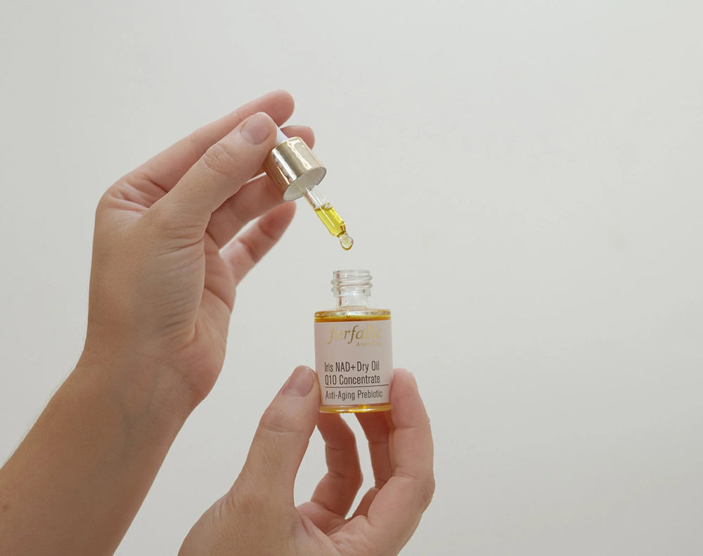 Hand hält farfalla Ölfläschchen mit Pipette und goldenem Anti-Aging Pflegeöl vor hellem Hintergrund