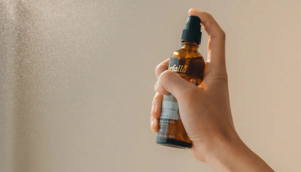 Hand sprüht farfalla Raumspray aus einer Braunglasflasche in die Luft